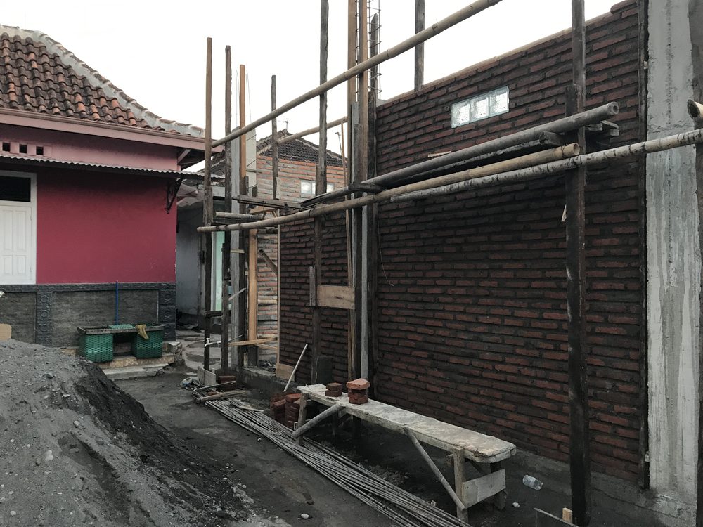 A new brick room with bamboo scaffolding being added beside an existing painted house